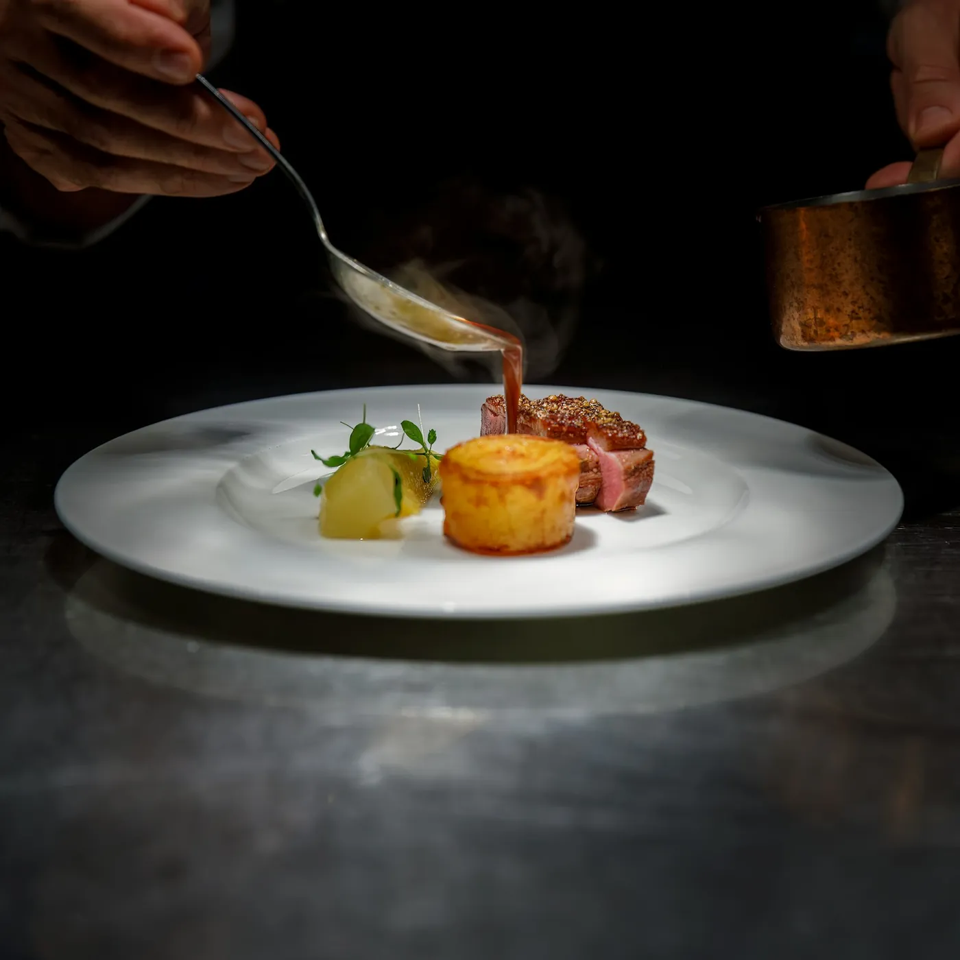 Plat d'autor acabat d'emplatar, amb un raig de salsa, sobre una taula fosca
